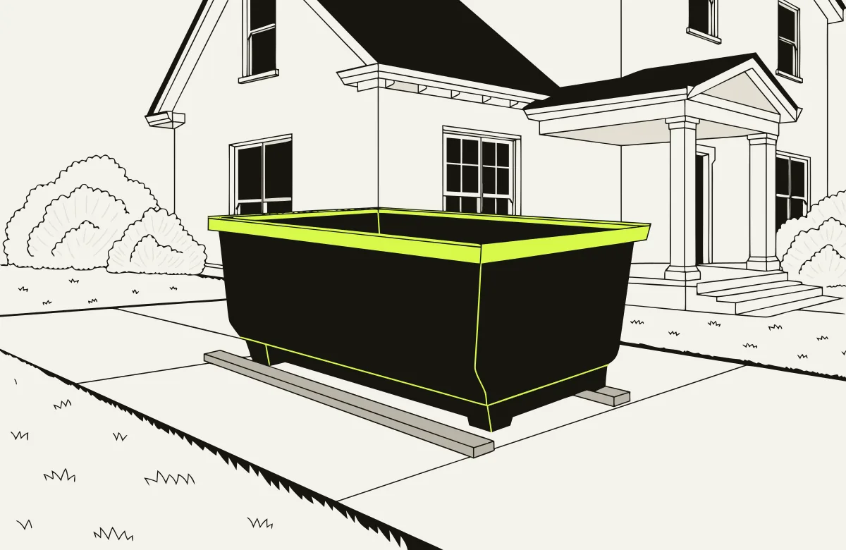 Roll-off dumpster on a home driveway resting on wooden boards that protect the pavement.